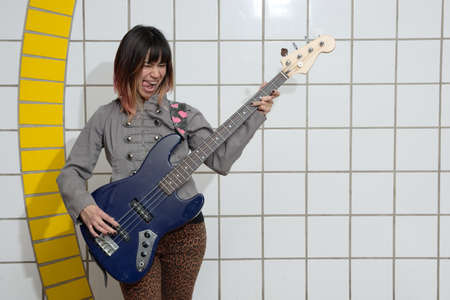 Female musician playing guitar in subway with tongue out