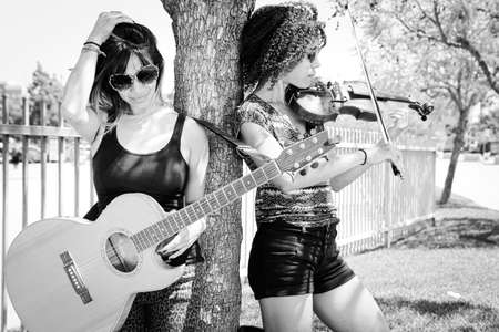Woman violinist and guitarist leaning against tree