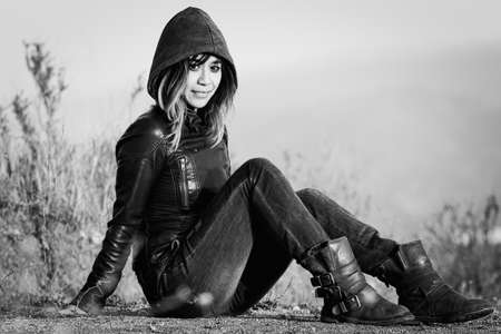 Woman seated on ground outside with hoodie and jacketの写真素材