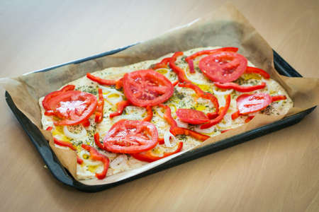Delicious fresh traditional Italian focaccia bread with tomatoes, red peppers, onions, basil and olive oil on pan ready to cookの写真素材