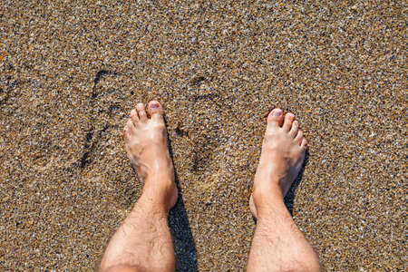 Male bare feet standing on the wet sandy beachの写真素材