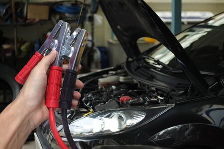 Hand holding Car battery charger over blurred car in garage background.
