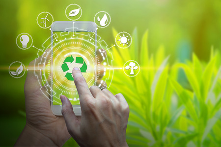 Hand holding smartphone with environment Icons over the Network connection on nature background, Technology ecology concept.の写真素材