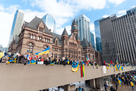 Toronto, Ontario, Canada â€“ February 27, 2022:  Protestors with banners and Ukrainian flags in...
