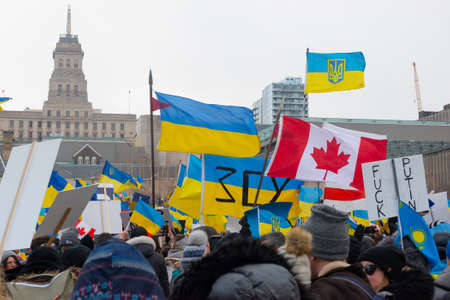 Toronto, Ontario, Canada â€“ February 27, 2022:  Protestors with banners and Ukrainian flags in...