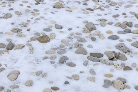 Small and large rocks lie scattered on the snowy ground, partially covered by a thin layer of white snow.の写真素材