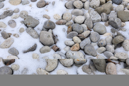 Small and large rocks lie scattered on the snowy ground, partially covered by a thin layer of white snow.の写真素材