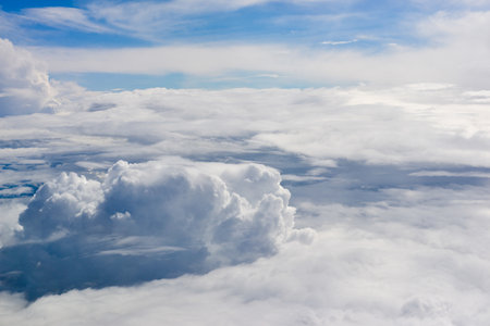 Vast blue sky surrounds massive cumulus clouds and bright sunlight as seen from above during an airplane flight over a scenic landscape.の写真素材