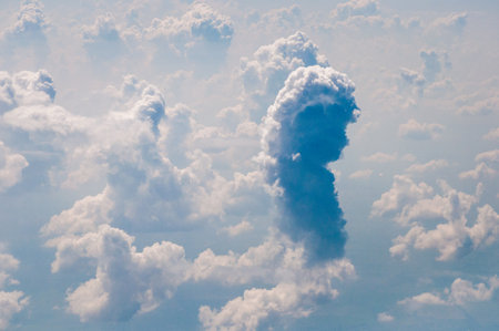 Vast blue sky surrounds massive cumulus clouds and bright sunlight as seen from above during an airplane flight over a scenic landscape.の写真素材