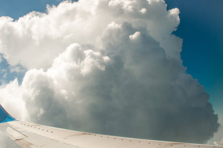 Vast blue sky surrounds massive cumulus clouds and bright sunlight as seen from above during an airplane flight over a scenic landscape.の写真素材