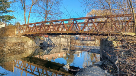 The Culham Trail Bridge spans a calm waterway, reflecting the structure and surrounding trees on a sunny day.の写真素材
