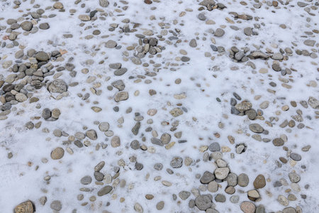 Small and large rocks lie scattered on the snowy ground, partially covered by a thin layer of white snow.の写真素材