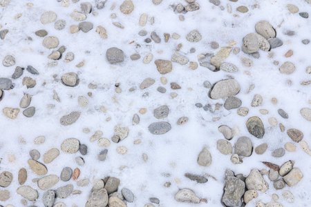 Small and large rocks lie scattered on the snowy ground, partially covered by a thin layer of white snow.の写真素材