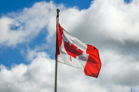 The red and white national flag of Canada with a maple leaf waves in the wind against a cloudy sky.の写真素材