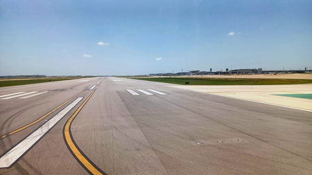 A long airport runway stretches towards the horizon under a clear, bright sky at a major...