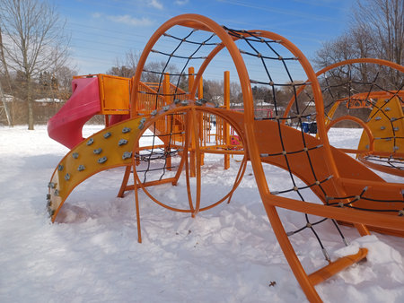 Toronto, ON, Canada - December 6, 2025: An orange metal and rope climbing structure stands empty in a children's playground covered with snow on a bright winter day.のeditorial素材