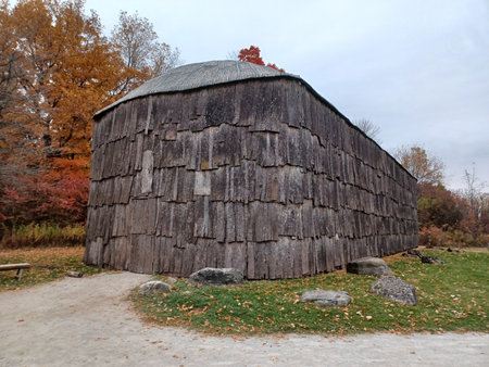 Ontario, Canada - July 5, 2025: A large historical longhouse building made of bark sits under a cloudy sky.の写真素材