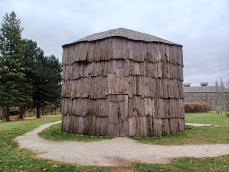 Ontario, Canada - July 5, 2025: A large historical longhouse building made of bark sits under a cloudy sky.の写真素材