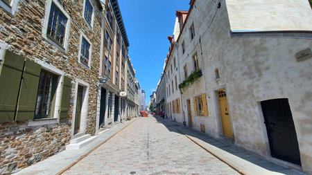 Montreal, QC, Canada - August 7, 2025: Quaint cobblestone street in Old Quebec City lined with historic buildings, showcasing charming windows and traditional shutters under blue skyのeditorial素材