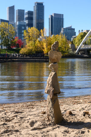 Rock cairn showing balance and stability, standing on a sandy beach with the Toronto skyline, autumn trees, and water of Lake Ontario creating a serene urban nature sceneの写真素材