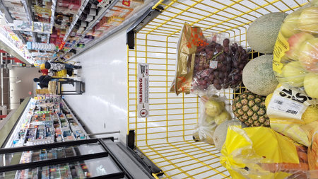 Toronto, ON, Canada - February 6, 2026: A yellow metal shopping cart contains various fresh fruits and vegetables while moving through a supermarket aisle.のeditorial素材