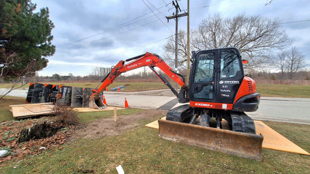 Toronto, ON, Canada - March 14, 2026: A Kubota KX080-4 excavator is parked on grass next to road...