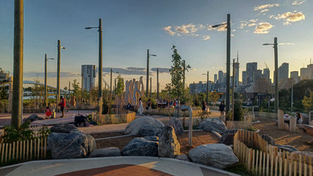 Toronto, ON, Canada - October 13, 2025: view at the Biidaasige Park in Toronto An urban park with wooden structures and people enjoys a colorful sunset against a city skyline.