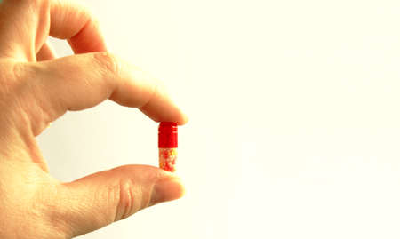 Hand holding the tablet between the thumb and forefinger. Capsule is white and red. Hand is located on the left side of the photo. Medicine. Taking drugs. Isolated. White background. FlatLayの写真素材