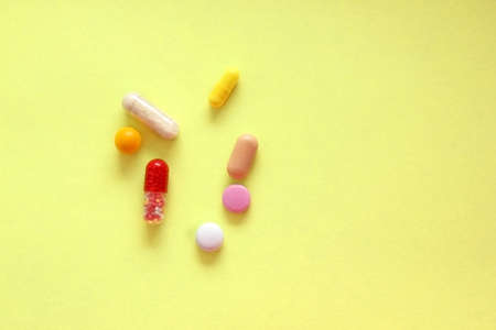 Multi-colored tablet lies on the yellow background on the left. Drug use. Treatment. Home first aid kit. Disease. Emergency services. View from above. Painkiller. Copying space for textの写真素材