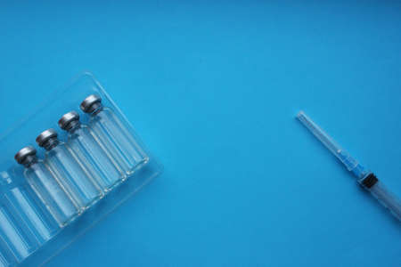 Ampoules of vaccine and a syringe on a blue background. Vaccination.