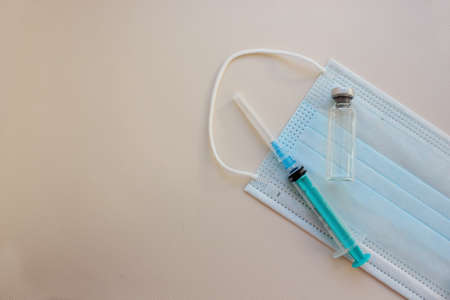 Syringe with needle, amulets with medicine lie on medical mask on light background. Vaccination. concept of medicine and immunity. Vaccination against viral infections. Flatly.Copy space.の写真素材