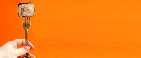 The hand holds a fresh sushi roll with a fork, insulated against an orange background. How to eat...