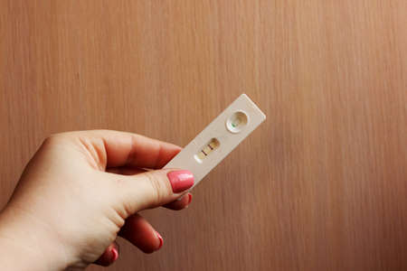 woman is hand holding positive pregnancy test on a light background. Motherhood, Pregnancy,...