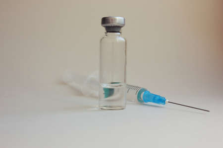A syringe with a needle, bottles of medicine lie on a medical mask on a light background. dicins and...