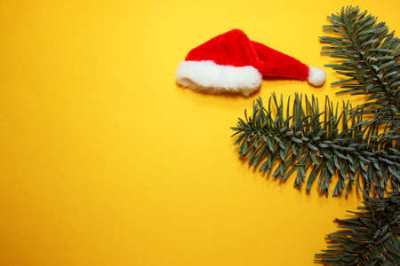 Santa Claus red hat and spruce branch on a yellow background. Symbol of Christmas and New Year. The headdress is festive. Located on the right. Top view. Copy Spaceの写真素材