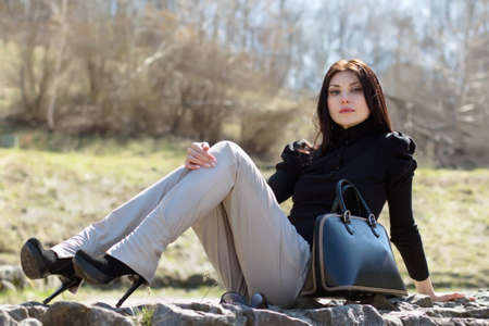 Attractive young brunette sitting on the rock with her black bagの写真素材