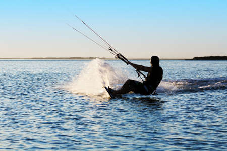 Silhouette of a kitesurfer sailing in the sea at sunset