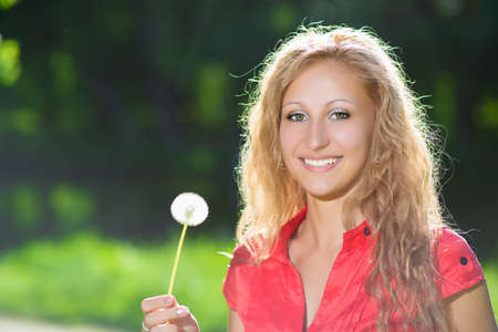Portrait of pretty cheerful blond woman posing with a dandelionの写真素材