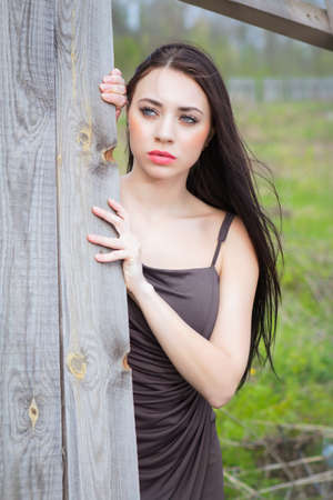 Pensive young brunette posing near the wooden fenceの写真素材