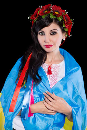 Young woman in wreath wrapped in Ukrainian flag. Isolated on blackの写真素材