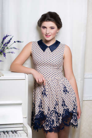 Attractive young woman in polka-dot dress posing near the pianoの写真素材
