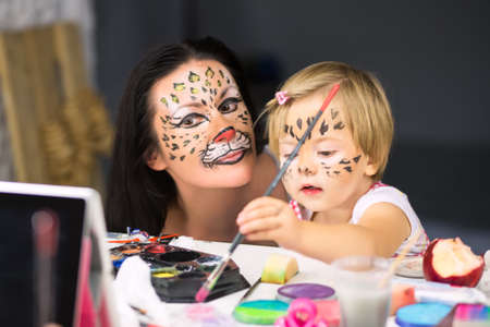Young woman looking at little girl painting in front of the mirror