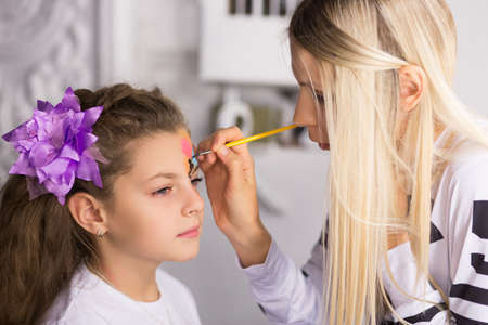 Blond woman paints the face of a girl
