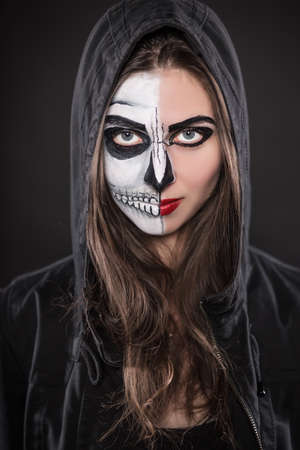 Portrait of young brunette in black hood with painted face for Halloween