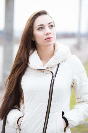 Portrait of attractive brunette in white jacket posing outdoors