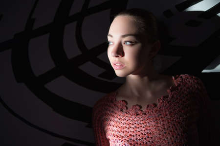 Portrait of thoughtful young lady wearing knitted sweater posing near wall