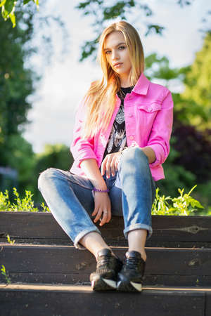 Nice young woman posing on the street, sitting on the stairs, wearing a pink jacket and pantsの写真素材