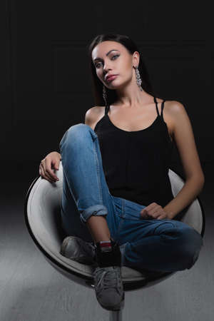 Sexy young lady on a black background sitting on a chair in the studio