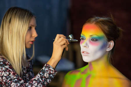 The artist puts a face painting on a lovely young model in the studio, against a gray wallの写真素材