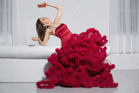 Nice lady posing in a studio posing on a sofa dressed in a gorgeous red dress and a crownの写真素材